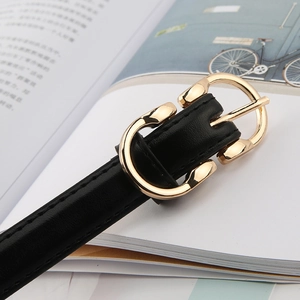 Close-up of black leather thin belt with gold horseshoe buckle on a book background