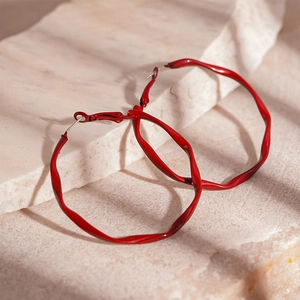 Close-up of red lacquer twisted wave hoop earrings on light stone surface