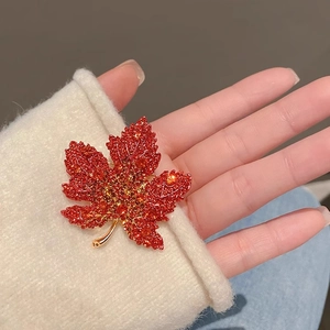 Detailed view of a red maple leaf brooch with crystals pinned on a white knit sweater cuff