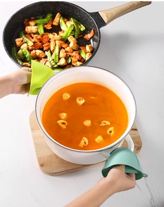 Green silicone heat-resistant oven mitts holding a white pot in a kitchen setting