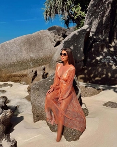 Detail of orange mesh beach cover-up and deep V swimsuit against seaside rocks