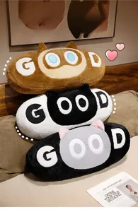 Three stacked long plush cat pillows with GOOD embroidery in a cozy bedroom setting