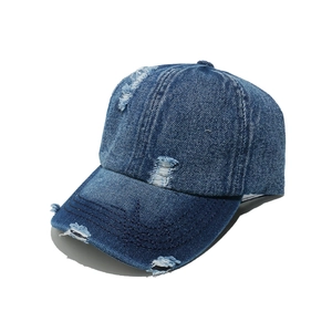 Detail of distressed dark blue denim baseball cap showing vintage frayed holes and texture