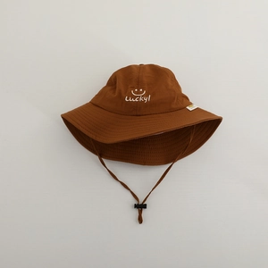 Detailed close-up of caramel bucket hat with lucky face embroidery and windproof cord