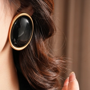 Close-up of vintage oval resin earrings with gold trim worn by a model in warm light