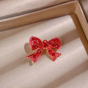 Macro detail of elegant red crystal bow brooch with gold setting on beige silk cushion