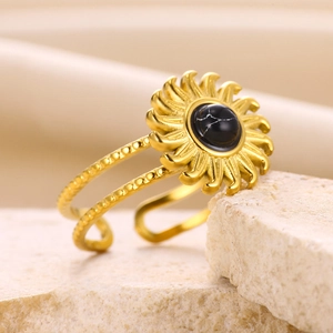 Detail of adjustable gold sunflower ring with black stone on beige rock base