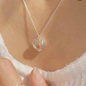 Detail of three-ring interlocking silver necklace pendant worn on a soft knit sweater