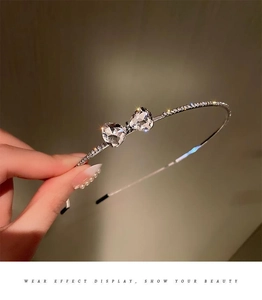 Detailed close-up of a silver metal headband with sparkling rhinestone bow embellishments