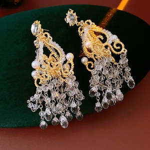 Detailed close-up of chandelier glass fringe earrings with pearls on green velvet