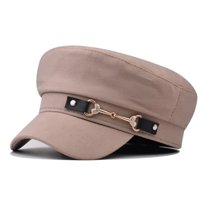 Detail of beige baker boy cap featuring a black decorative band and gold bit buckle
