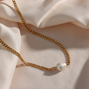 Detail of freshwater pearl pendant on a gold cuban chain against pink silk background