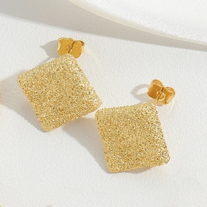 Macro detail of square gold earrings featuring stardust texture and a polished finish