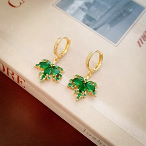 Detail of gold maple leaf earrings with green zircon stones on vintage book background