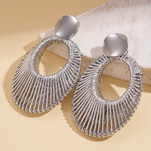 Detailed view of silver braided oval earrings with woven cable texture on marble base