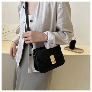 Detail of elegant black leather crossbody bag with a wavy flap and gold rotary lock