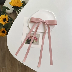 Detail of pink satin ribbon bow hair clip with long streamers on a floral desk