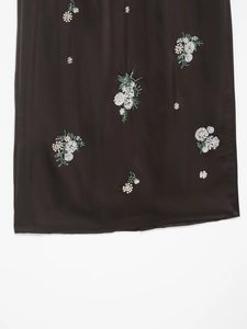 Détail de paillettes et broderie fleurie sur jupe en satin sombre avec perles à l'ourlet