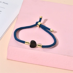 Close-up of adjustable blue braided rope bracelet featuring a black heart charm and gold beads