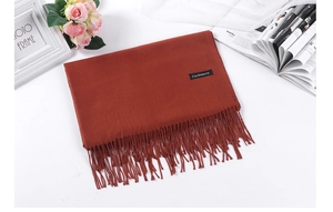 Close-up of orange-brown cashmere scarf with fringes on a styled white table