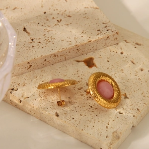 Gros plan détaillé de boucles d'oreilles dorées martelées avec gemmes roses sur pierre