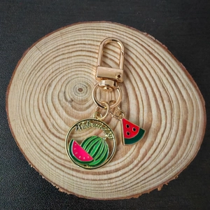 Cartoon watermelon keychain with gold clip and metal charm on rustic wooden base
