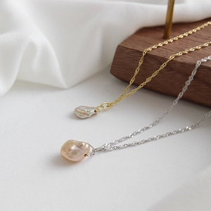 Detail of silver and gold twisted rope chains with natural baroque pearls on wood surface