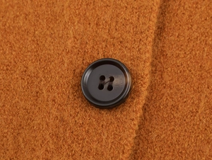 Macro de la texture du tricot orange et du bouton marron foncé à quatre trous du gilet