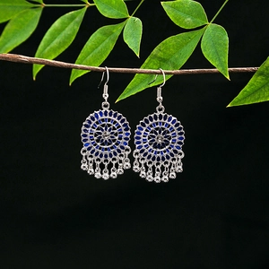 Detail of ethnic silver alloy earrings with blue floral hollow pattern and metal tassels