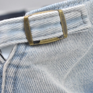 Detailed close-up of antique bronze metal buckle on light blue denim washed beret cap