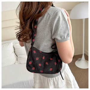 Detailed close-up of a black corduroy shoulder bag featuring red strawberry patterns