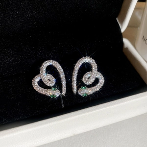 Macro shot of silver snake heart earrings with sparkling zircons and green stone eyes