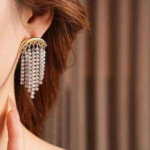 Close-up of model wearing gold tassel earrings with sparkling rhinestones and moon design