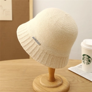 Minimalist cream knit bucket hat with striped brim and silver metal fashion tag