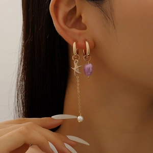 Close-up of asymmetric gold earrings with a purple heart pendant and starfish chain