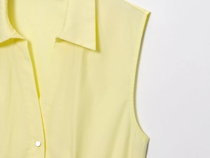 Detail view of light yellow sleeveless poplin top featuring lapel V-neck and single button