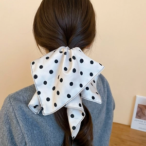 Dettaglio di un elastico per capelli bianco a pois neri legato a fiocco tra i capelli