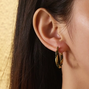 Detail of gold twisted hoop earring featuring inlaid green crystals on a model