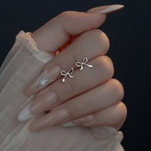 Detailed view of silver bow-shaped stud earrings held between fingers with elegant manicure