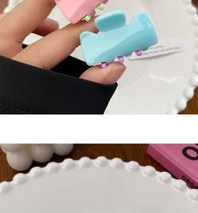 Close-up of pastel macaron-colored hair clips held over a decorative ceramic plate