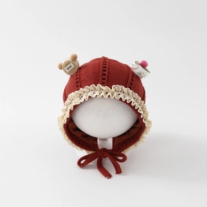 Detail of baby knit hat in red with cream lace trim and bear smile charm