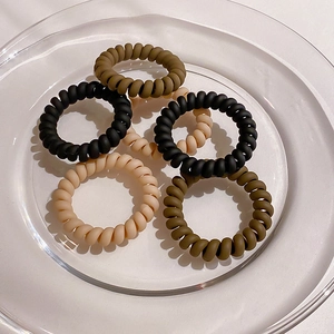 Detail view of five matte spiral hair ties in earthy tones on a clear glass plate