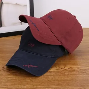 Detail of embroidered cotton baseball caps in burgundy and navy blue on a wooden table