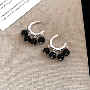 Close-up of C-shaped silver earrings with black beads on textured fabric background