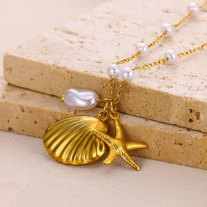 Gold stainless steel ocean necklace with shell and starfish charms on stone pedestal