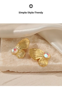 Detail of golden butterfly wing earrings with opal gemstone on beige stone and silk