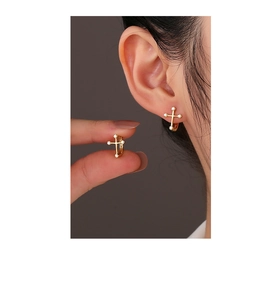 Detail showing asymmetric gold-plated cross hoop earrings with white zircon stones