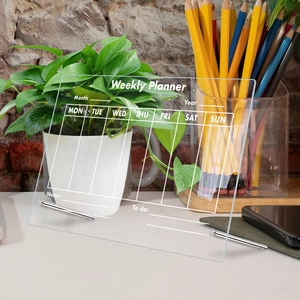 Clear acrylic weekly planner with silver stands on a desk showing Mon-Sun and notes section