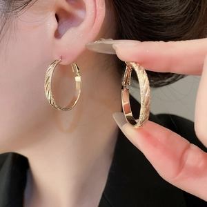 Detail of golden textured hoop earrings with a matte finish and polished edges on model