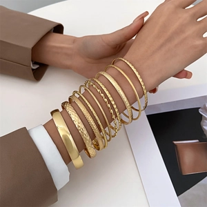Close-up of a stacked gold bracelet set with polished, textured, and twisted patterns